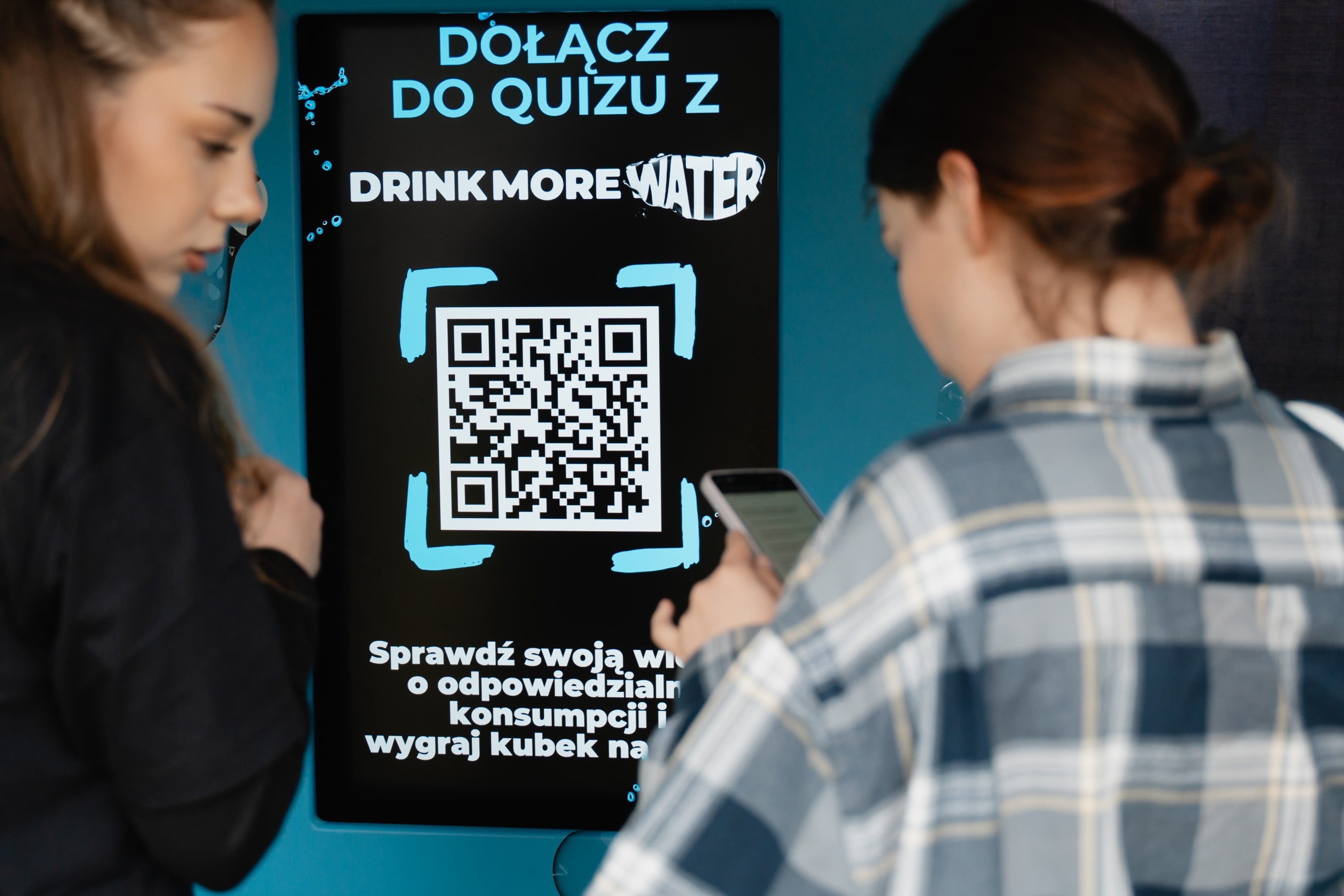 Dwie dziewczyny skanują kod QR, by dołączyć do quizu Drink More Water