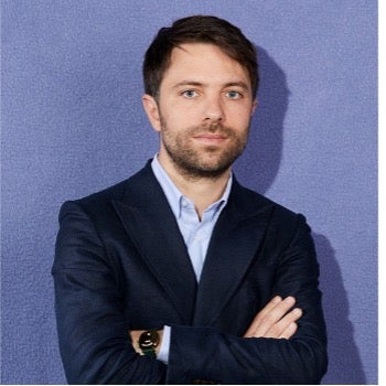 Headshot of Nicolas Oudinot, wearing a dark suit with shirt with arms crossed 