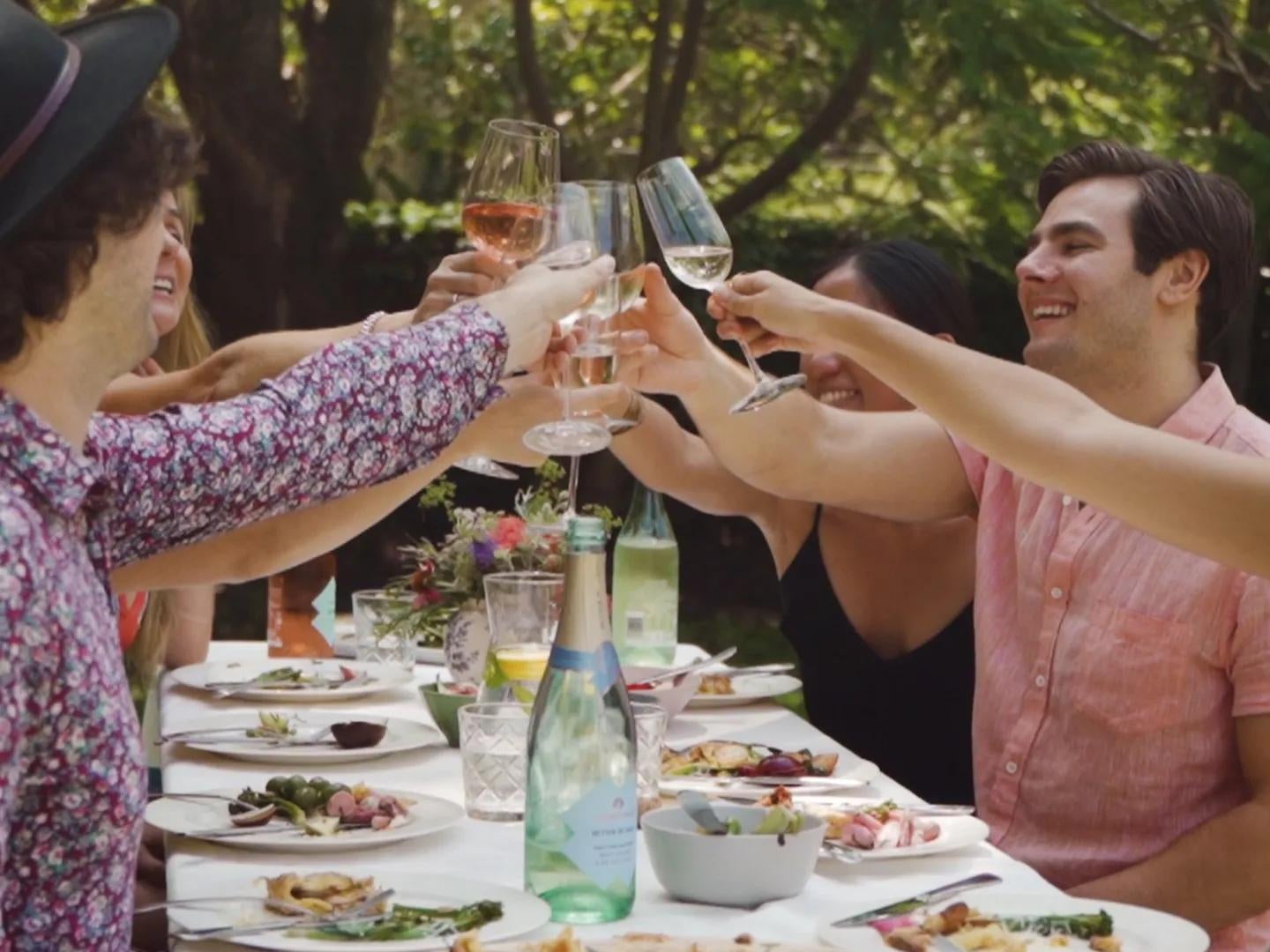 Friends celebrate a toast while having a meal seated at a table in a garden.