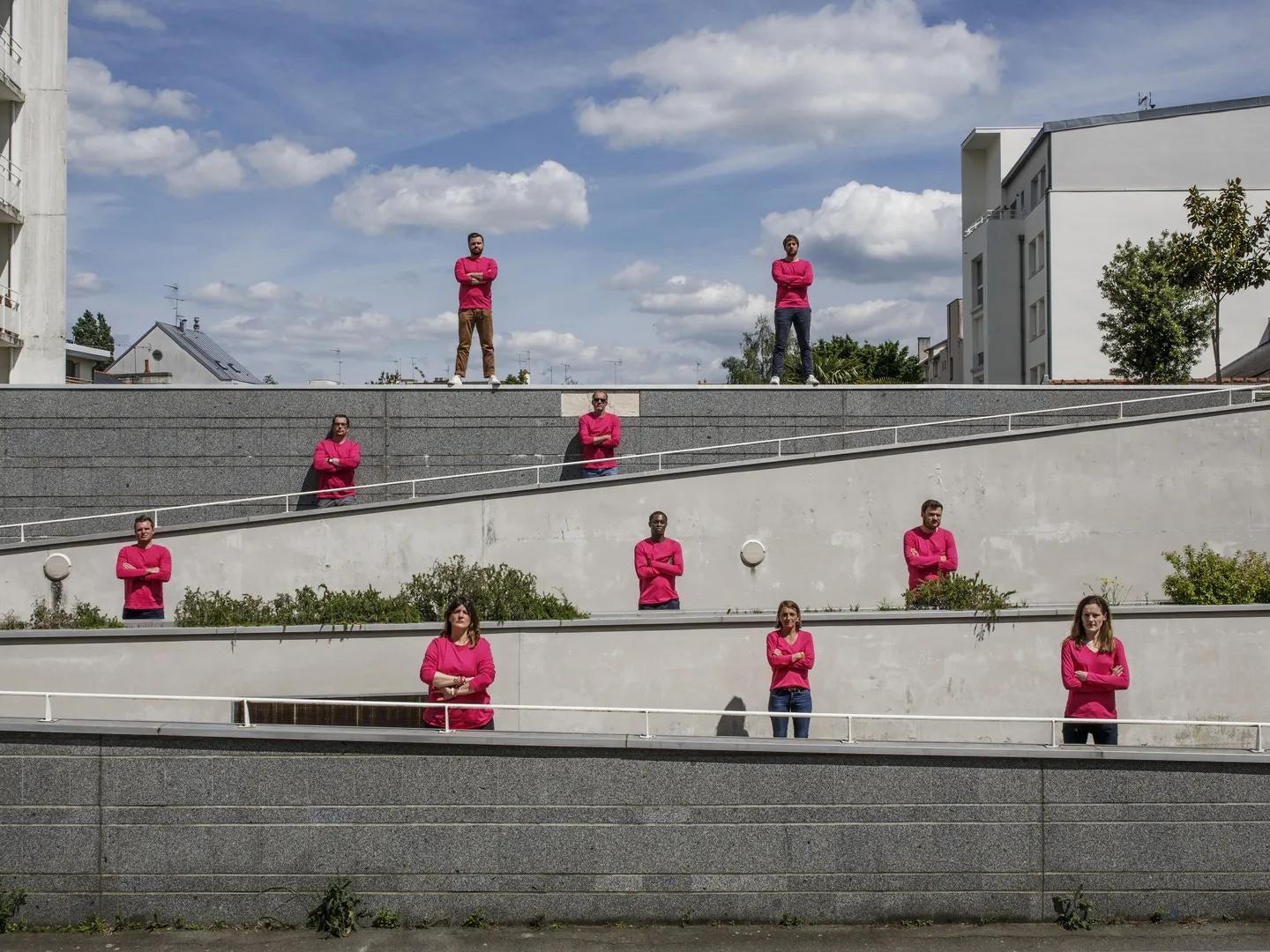 Ten people in matching pink tops stand apart in a lined formation along stairs