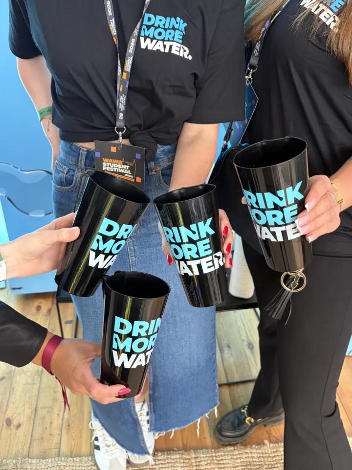 Zdjęcie osób wyciągających kubki z napisem "drink more water"