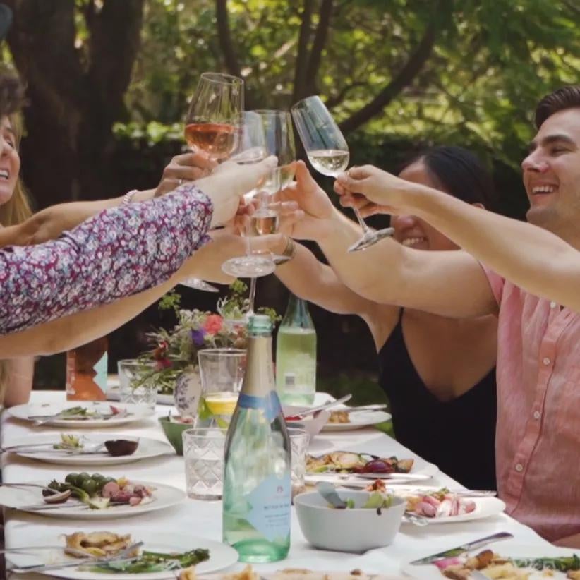 Friends celebrate a toast while having a meal seated at a table in a garden.