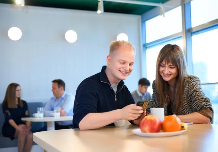 two people are sitting at a table and looking at the phone