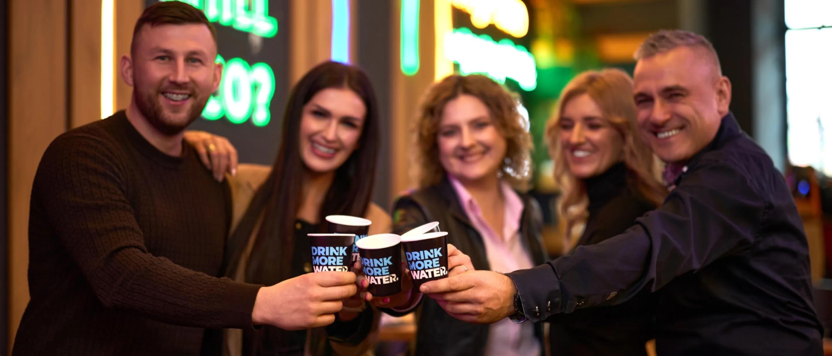 dwóch mężczyzn i dwie kobiety trzymają kubeczki z logo drink more water